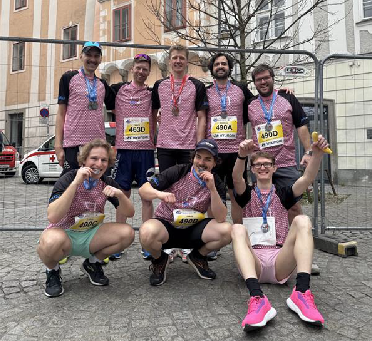 Team aus 8 Personen in Sportklamotten, die ihre Medaillen präsentieren.